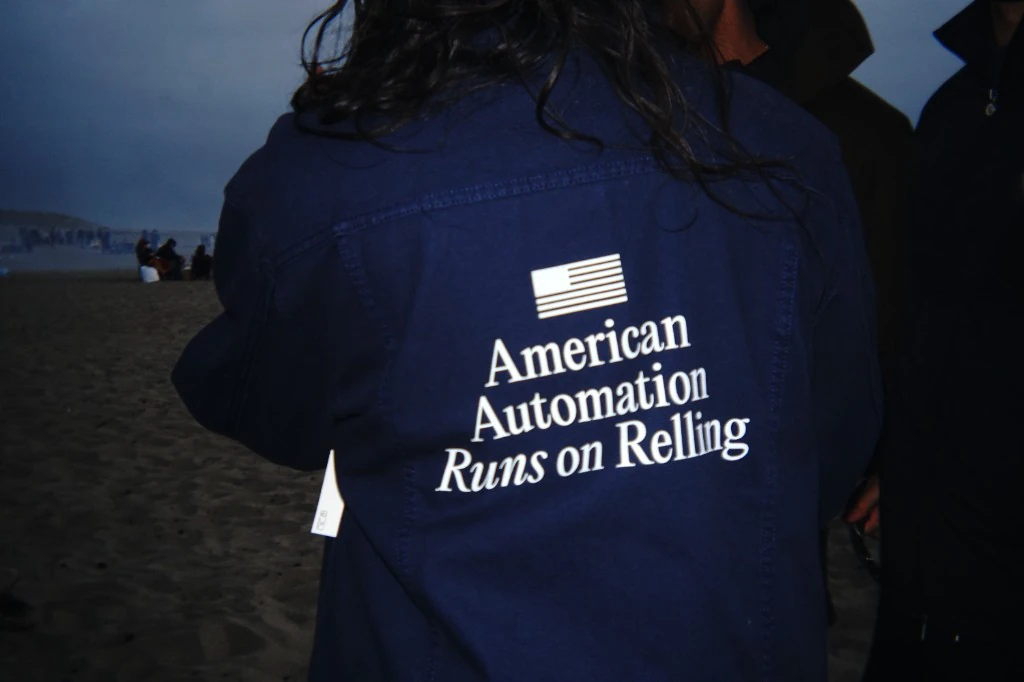 Back of the navy Relling company jacket, screen-printed American Automation / Runs on Relling, worn on a beach at dusk